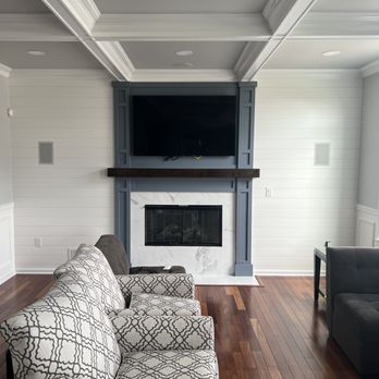 Modern living room with fireplace, TV mounted above, hardwood floors and coffered ceiling