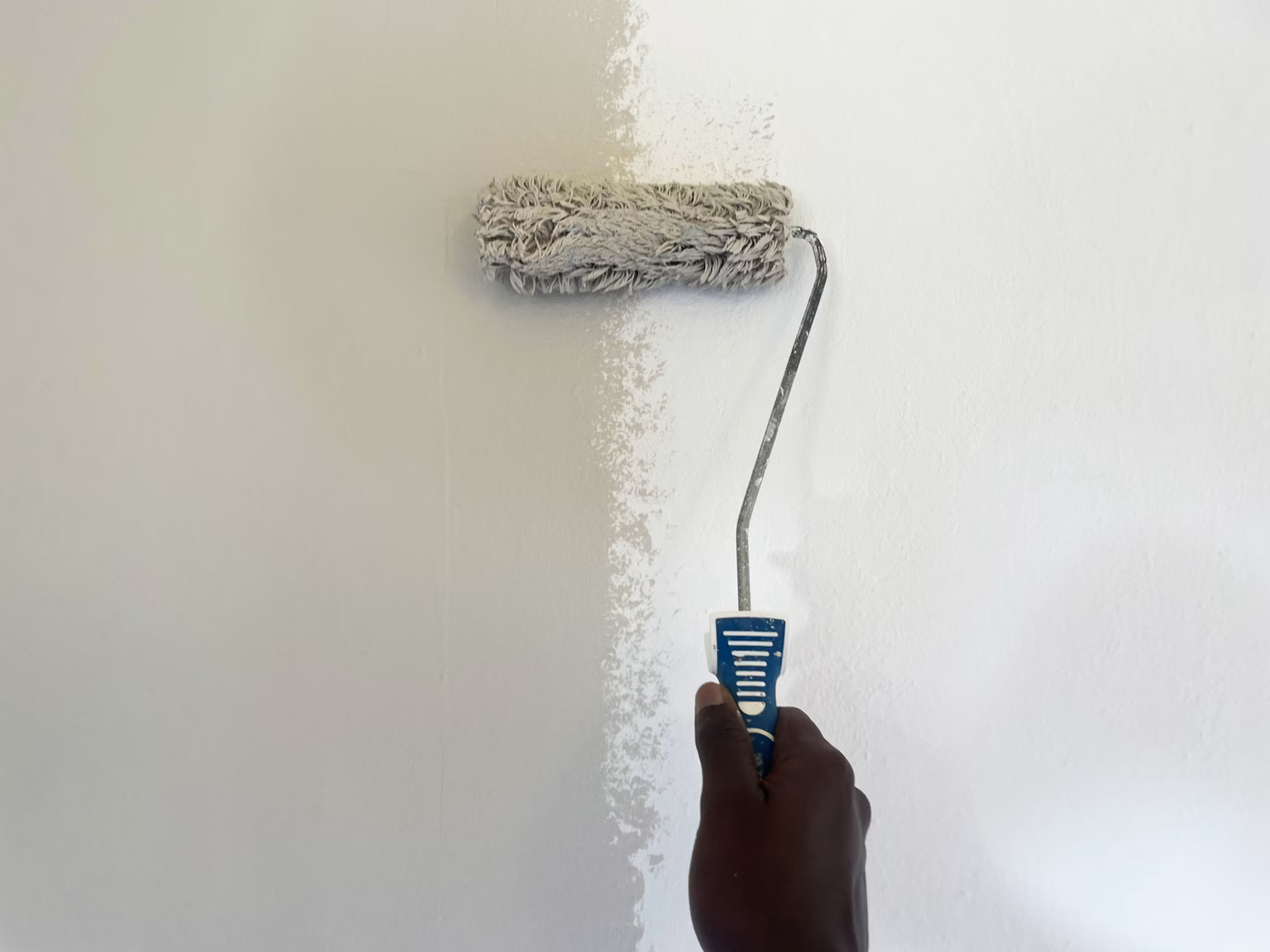Person holding paint roller with textured roller cover applying white paint to wall
